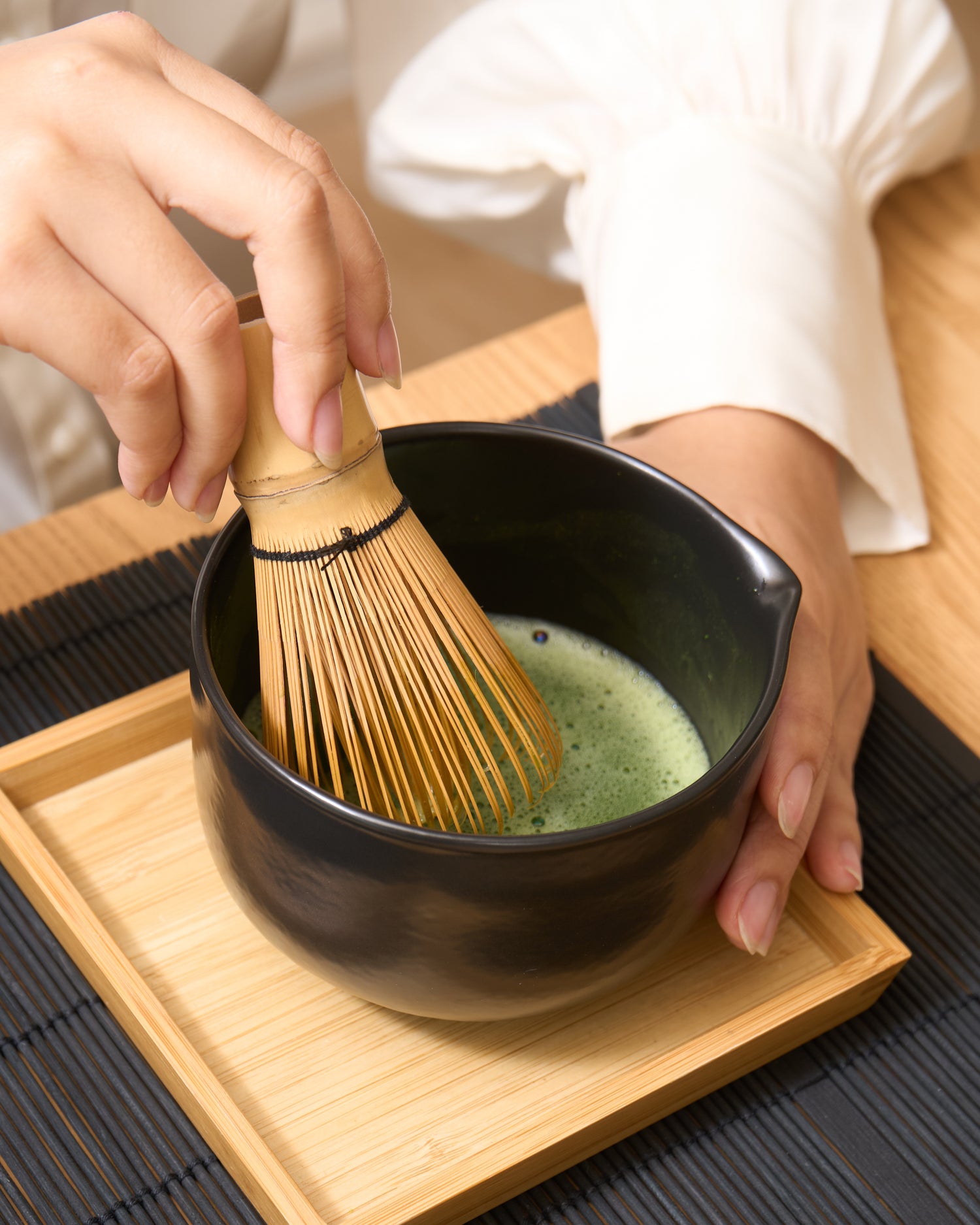 Une jolie main de femme tenant un fouet chasen dans sa main droite et préparant un matcha usucha dans un bol traditionnel chawan.