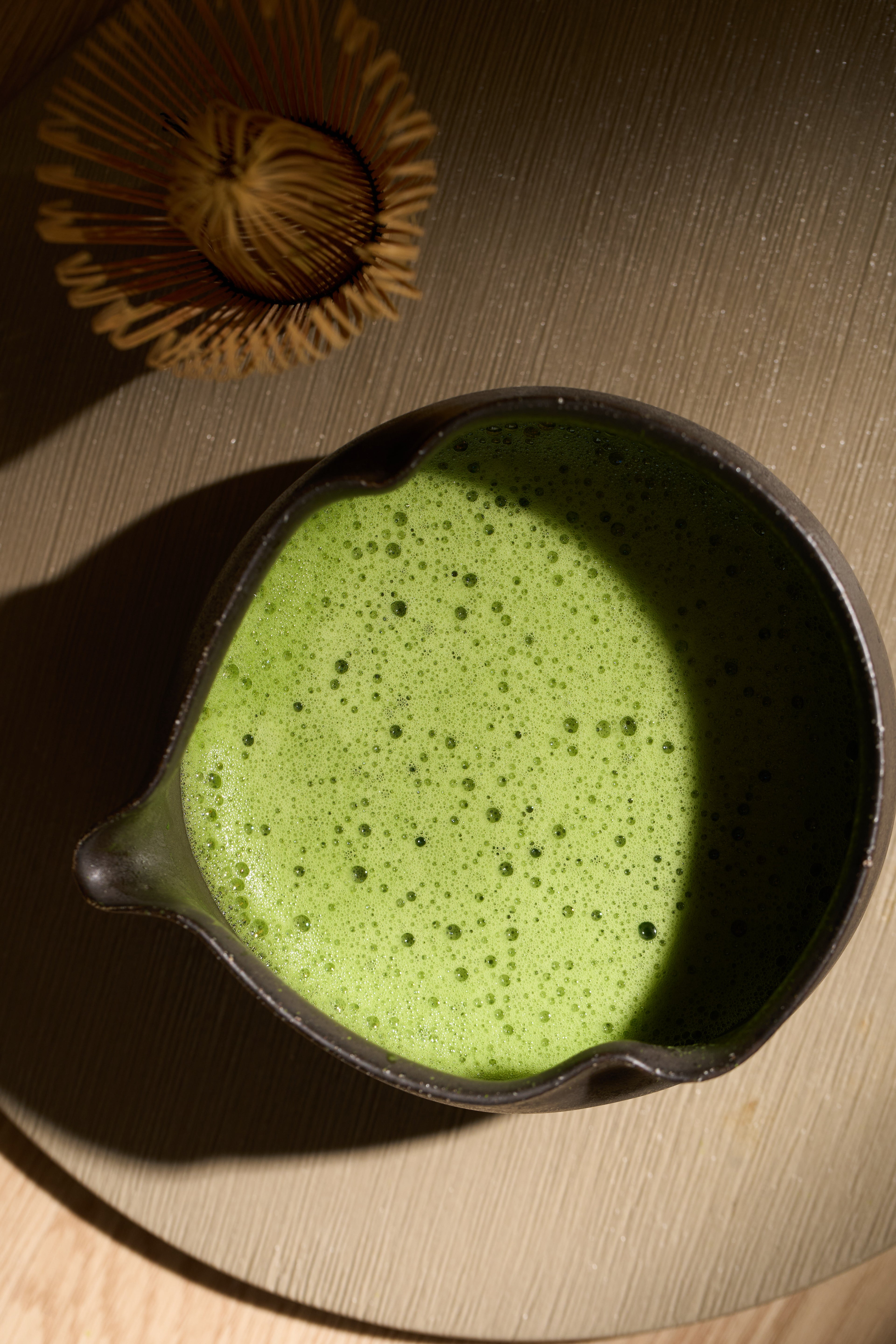 Bol de matcha vu de dessus, montrant une belle mousse verte caractéristique d'une préparation Usucha, éclairé par la lumière du soleil avec des ombres délicates.