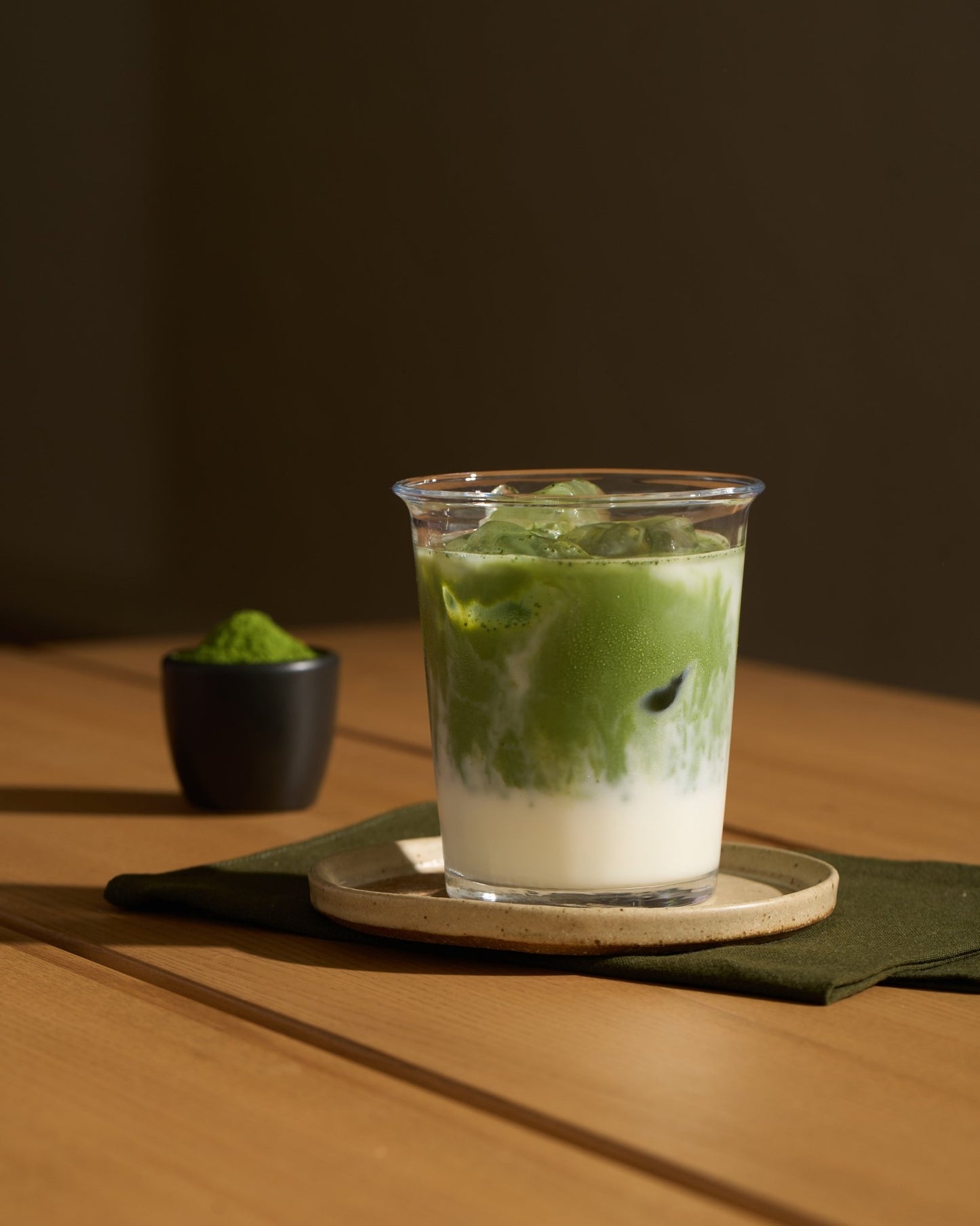 matcha latte dans un verre avec une coupelle remplie de matcha en arriere plan.