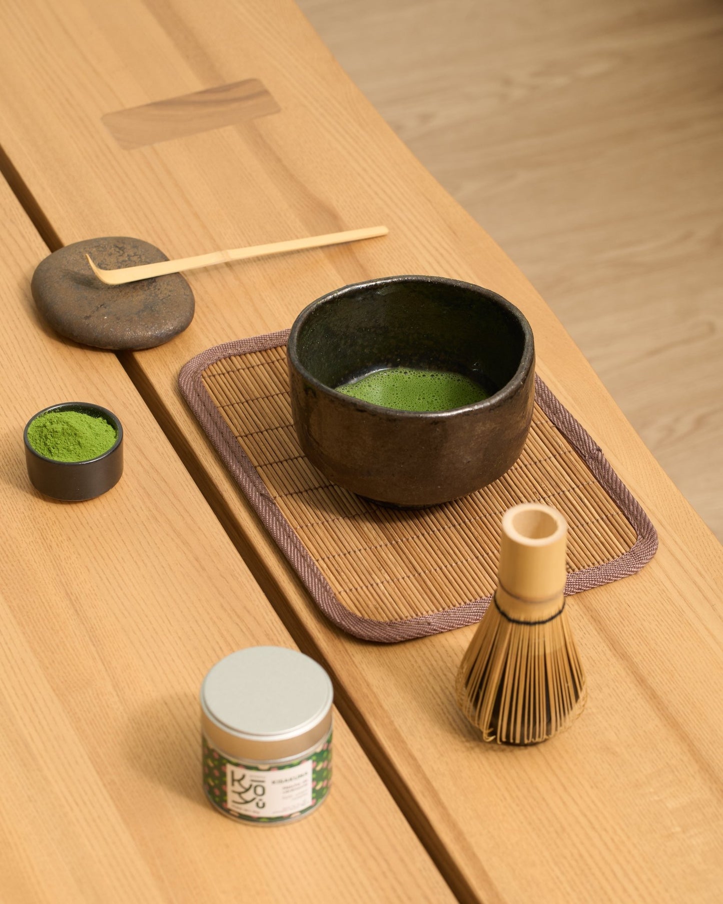 Bol de matcha avec une préparation Usucha, autour duquel sont disposés un fouet (chasen), une cuillère en bamboo traditionnelle et une coupelle remplie de poudre de matcha.